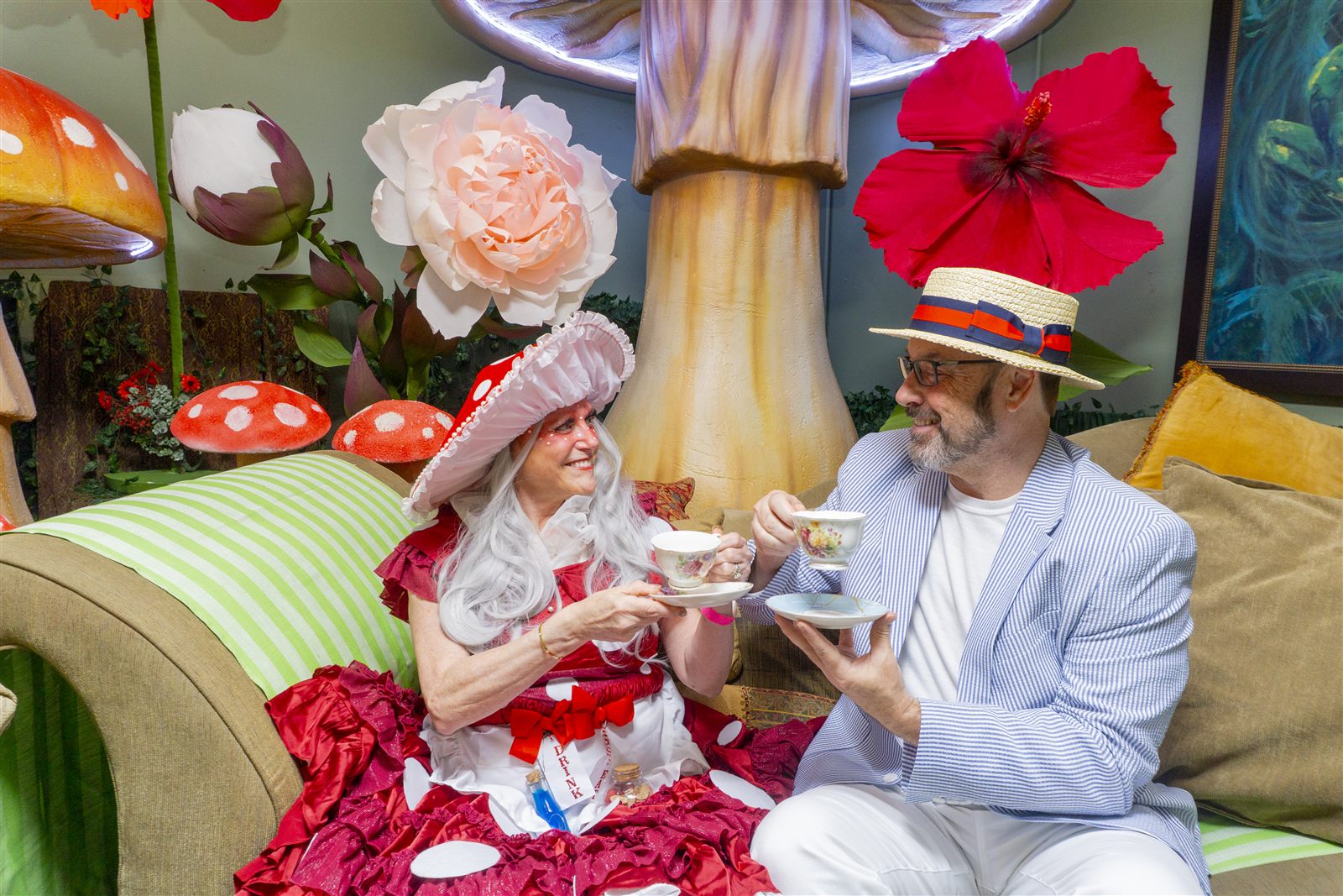 Guests in Wonderland costume toasting with floral teacups among oversized mushrooms