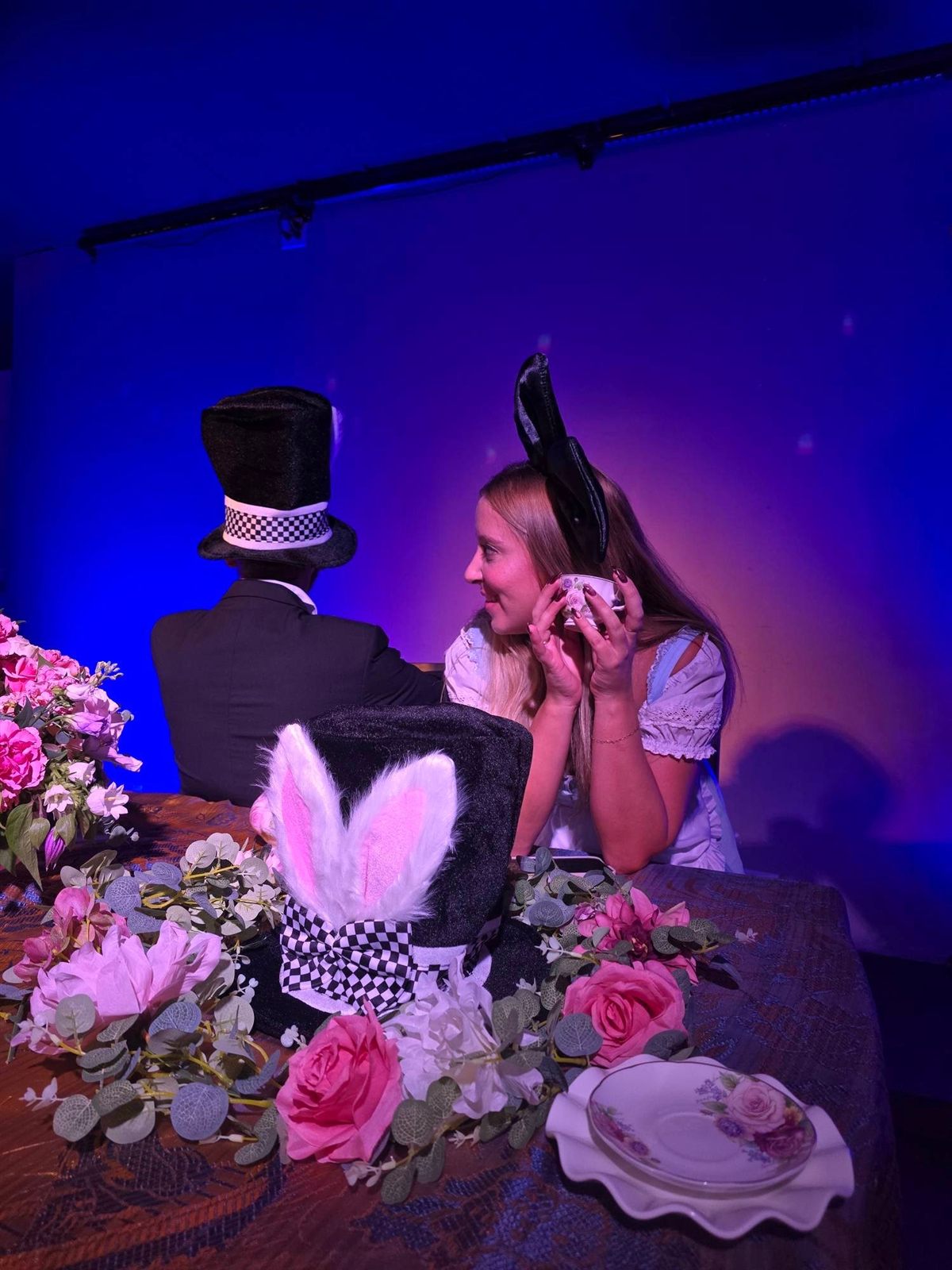 Alice-inspired tea with a bunny-eared top hat, roses, and guests in costume