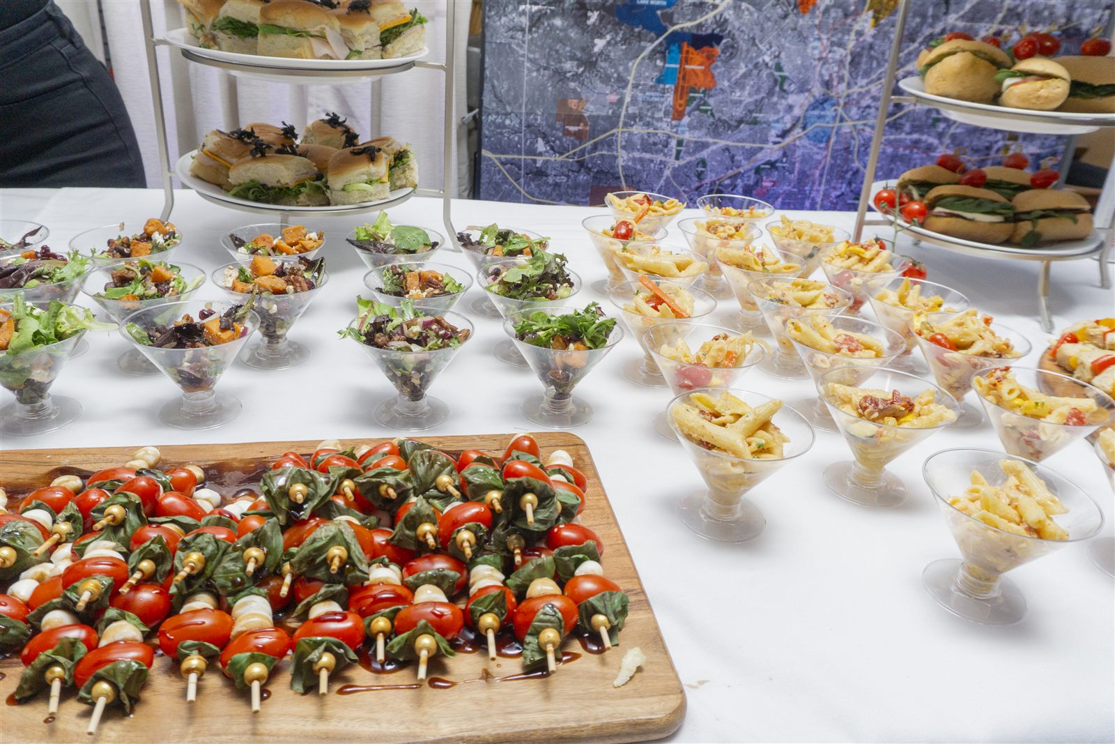 Catering spread with tea sandwiches, salads, and caprese skewers